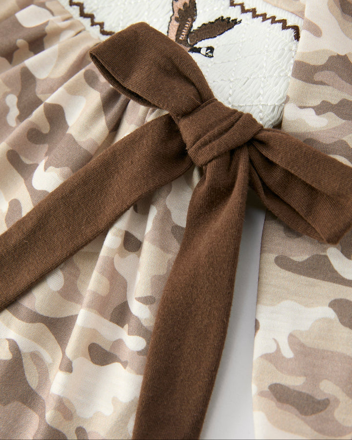 Camouflage-patterned fabric with a brown ribbon tied in a bow.