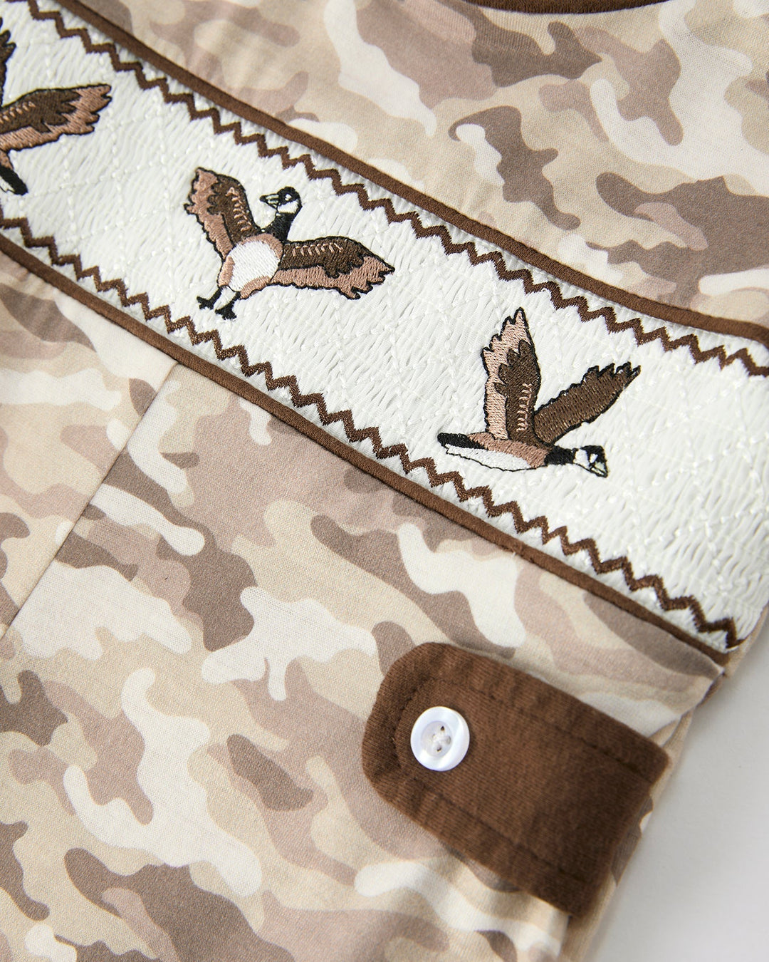 Camouflage-patterned fabric with embroidered birds and a button detail.