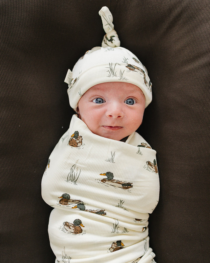 White ribbed newborn knot hat with duck print, baby facing forward