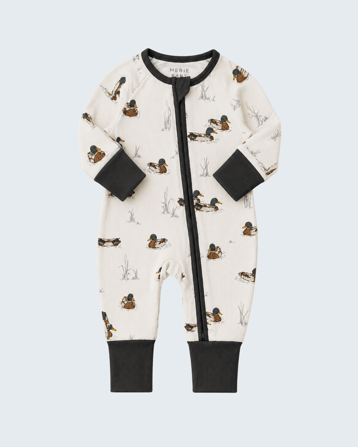 A baby long-sleeve footless one-piece sleeper with a front zipper, featuring an off-white background with a printed pattern of ducks and reeds, finished with black cuffs, collar trim, and zipper trim.