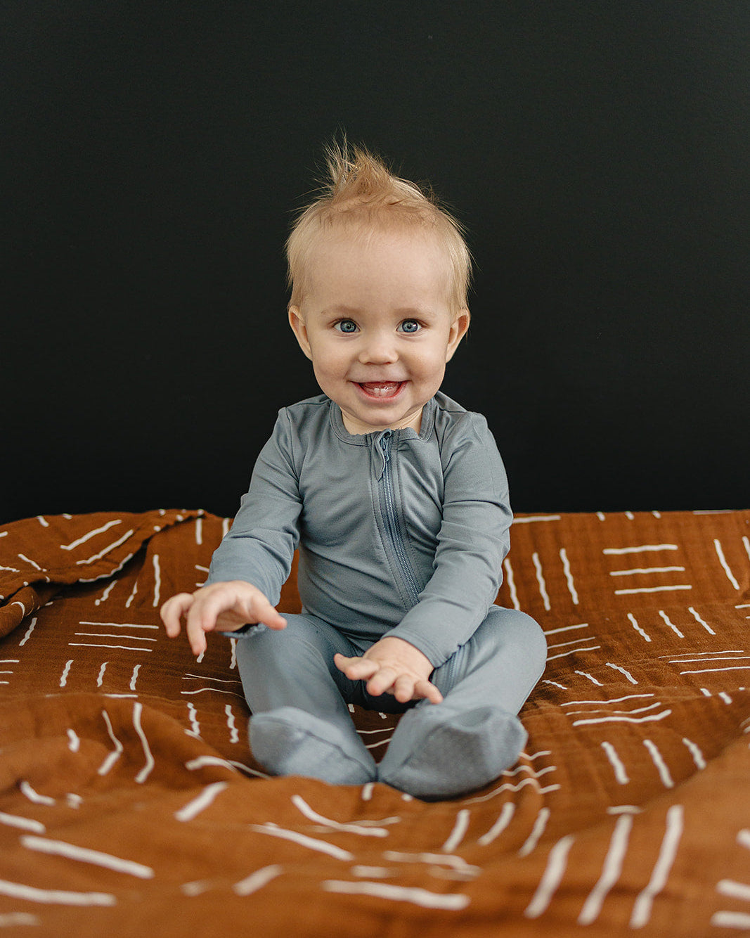 Child sitting on a patterned blanket against a black background