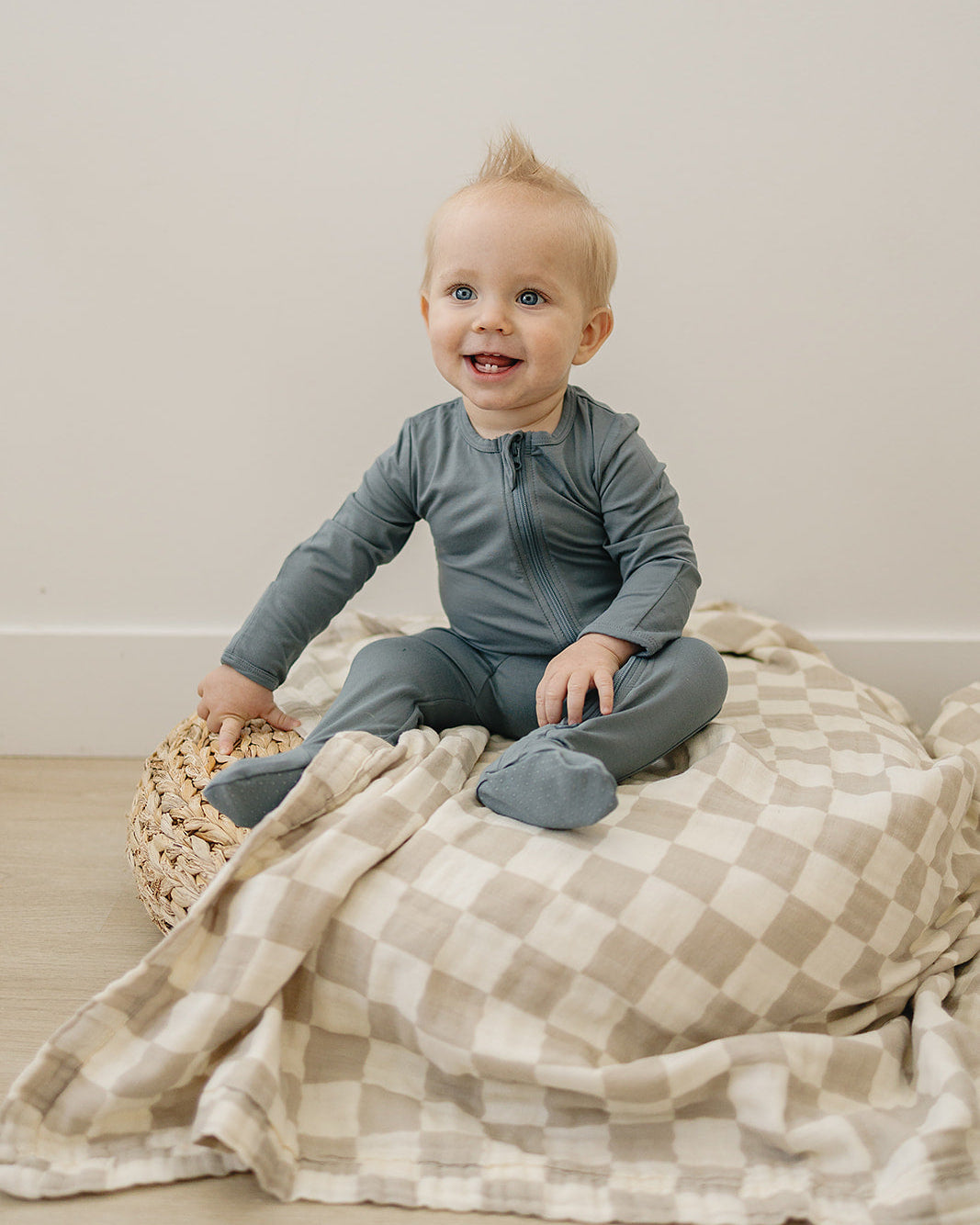Baby sitting on a checkered blanket with a neutral background