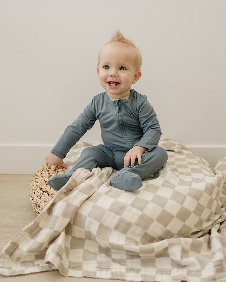 Baby sitting on a checkered blanket with a neutral background