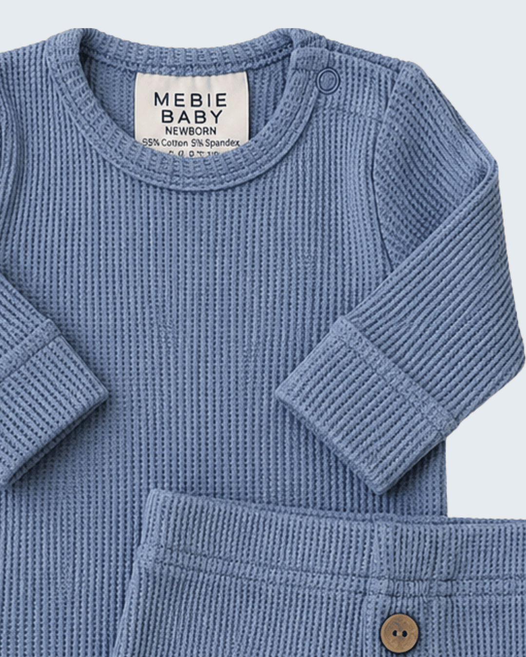 A close-up of a baby knit two-piece outfit in dusty blue, featuring a long-sleeve crewneck top and matching pants with a wooden button.
