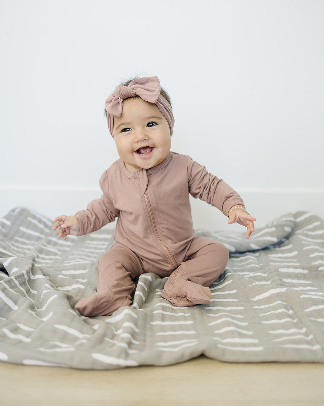 Baby in a pink outfit with a headband sitting on a textured blanket.