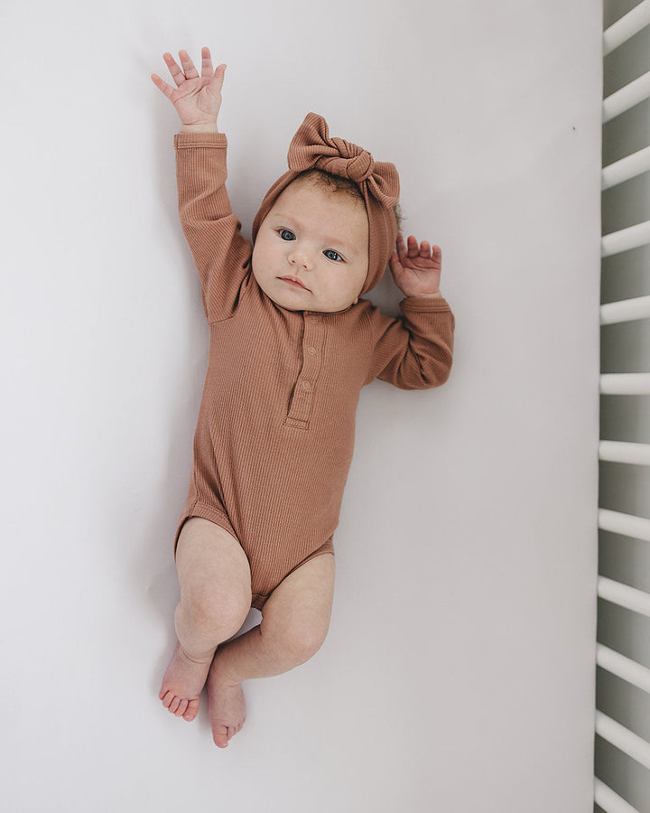 Baby in a brown onesie with a bow on a white background