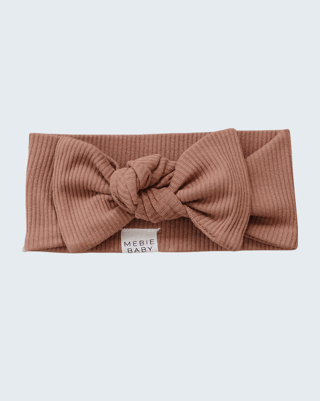 A ribbed knit headband in a dusty rose-brown color, featuring a large central knot bow and a small white fabric label that reads &