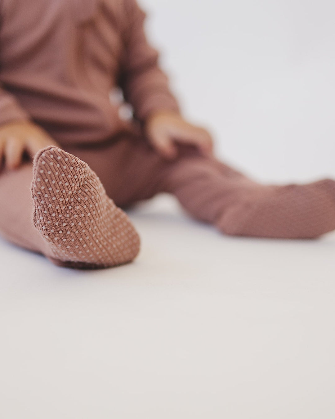 Baby feet in dusty rose ribbed zipper romper with textured fabric cuffs