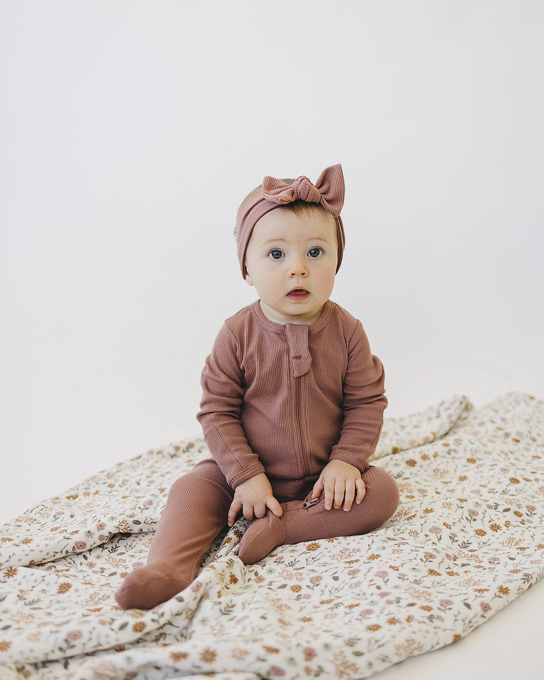 Dusty rose ribbed zipper romper on a baby sitting on a floral mattress
