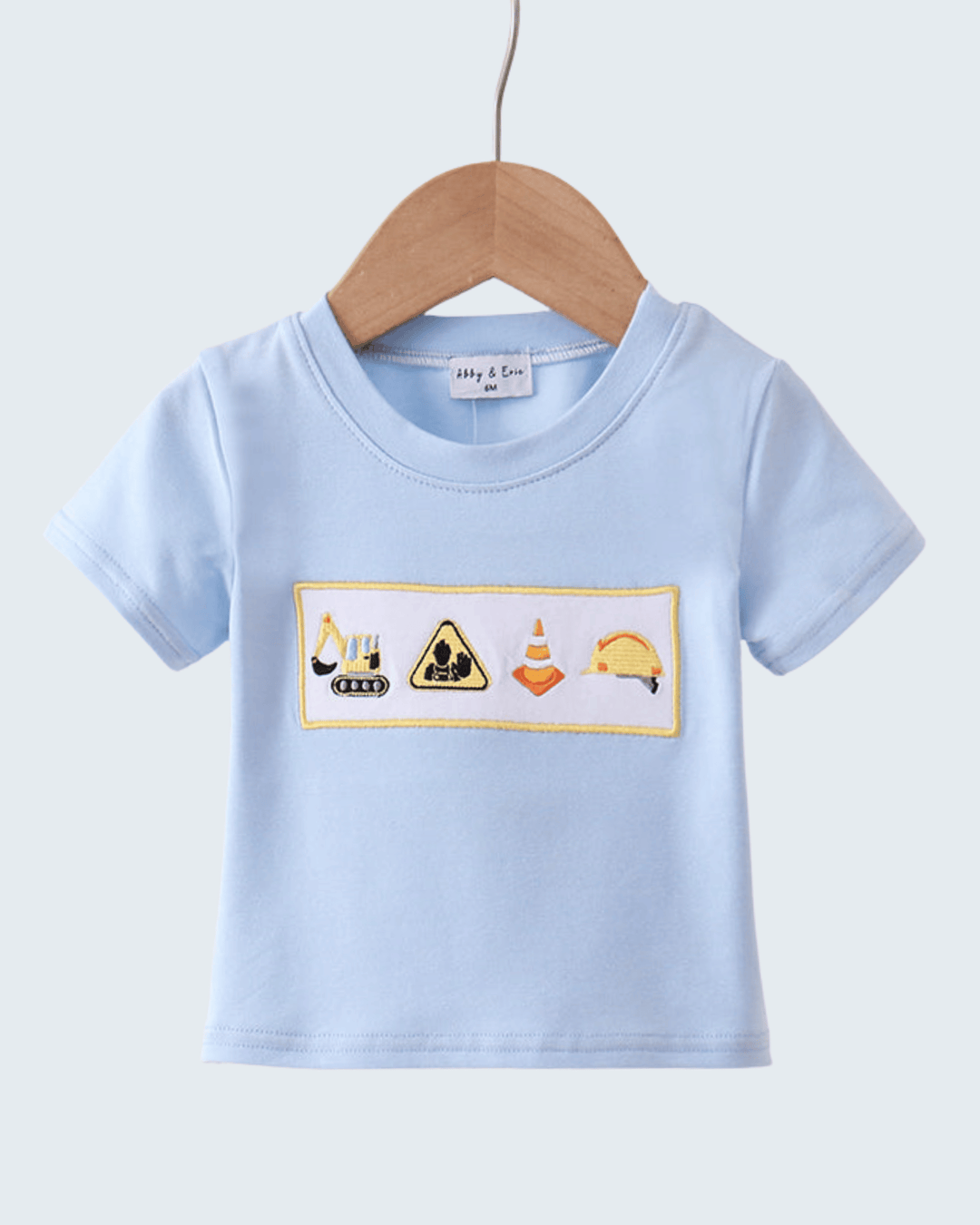 Light blue t-shirt with construction-themed design on a hanger against a light gray background