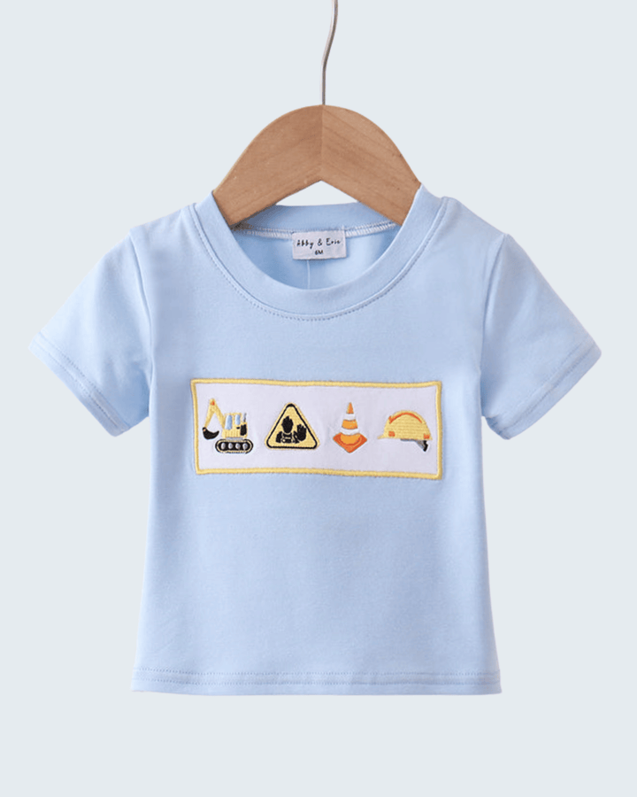 Light blue t-shirt with construction-themed design on a hanger against a light gray background