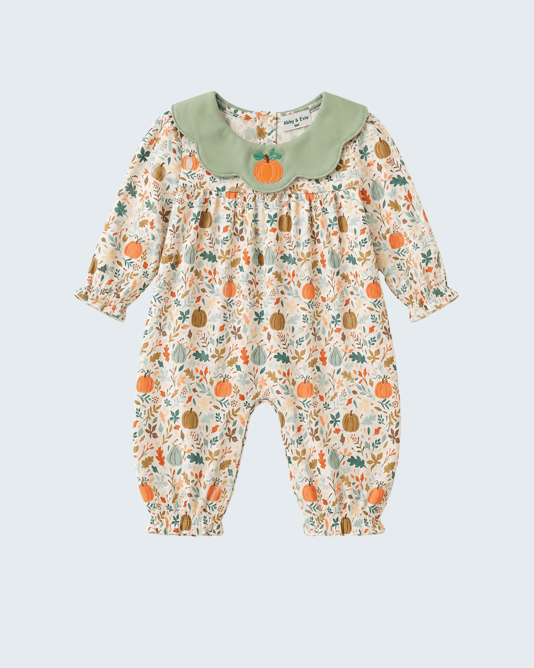 A baby long-sleeve romper with a cream base, an all-over autumn pumpkin and leaf print, and a contrasting sage green Peter Pan collar featuring a small embroidered orange pumpkin.
