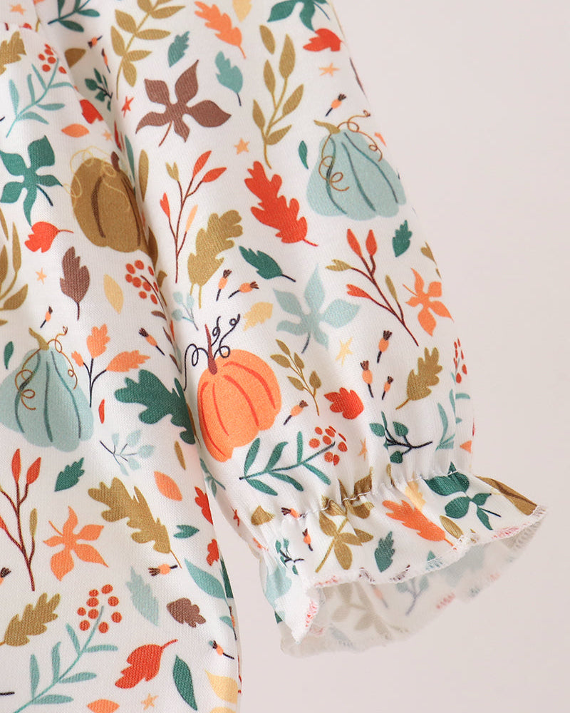 A close-up of a white blouse with a colorful autumn print featuring pumpkins, leaves, and berries, styled with a ruffled cuff.