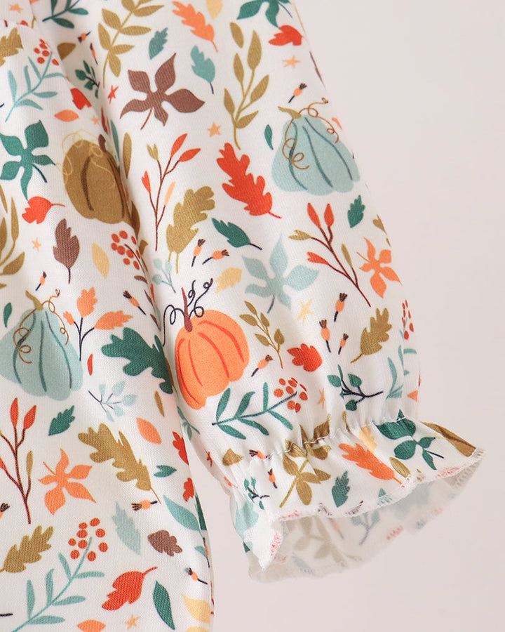 A close-up of a white blouse with a colorful autumn print featuring pumpkins, leaves, and berries, styled with a ruffled cuff.