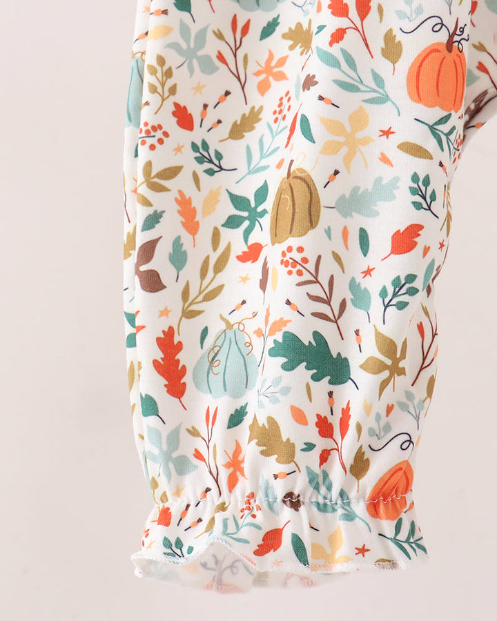 A close-up of a white fabric garment with a colorful autumn print featuring pumpkins, leaves, and flowers, finished with a ruffled hem.