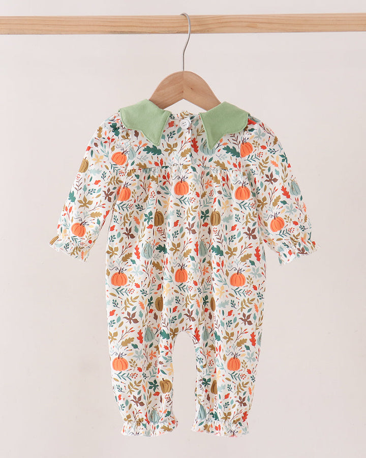 A baby long-sleeve footless romper hanging on a wooden hanger against a plain light background. The romper has an off-white base with a dense autumn leaf and pumpkin print in orange, green, and brown, and features a contrasting light green collar.