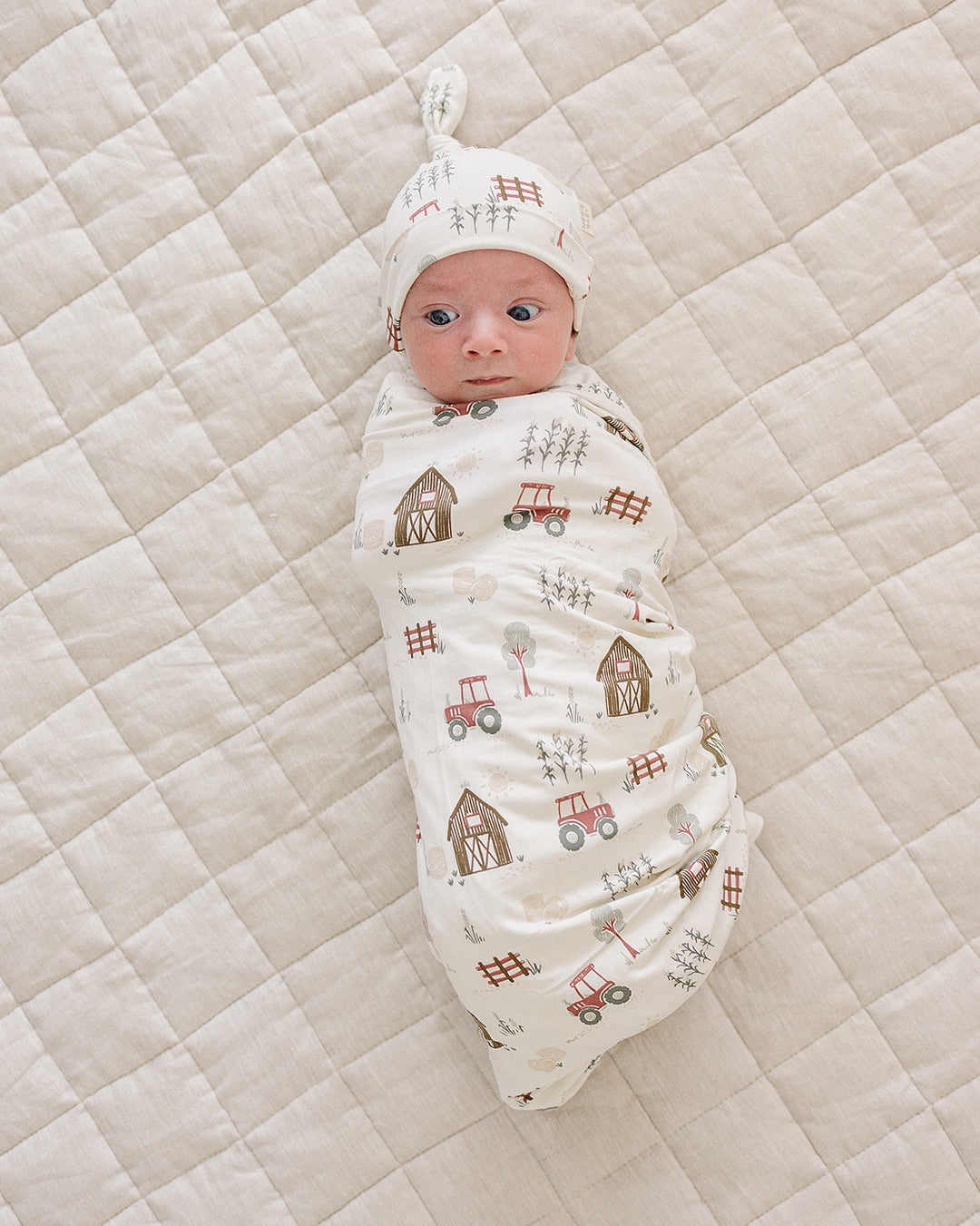 Newborn knot hat and farm patterned outfit on baby lying on quilt