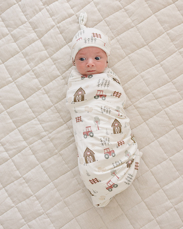 Newborn knot hat and farm patterned outfit on baby lying on quilt