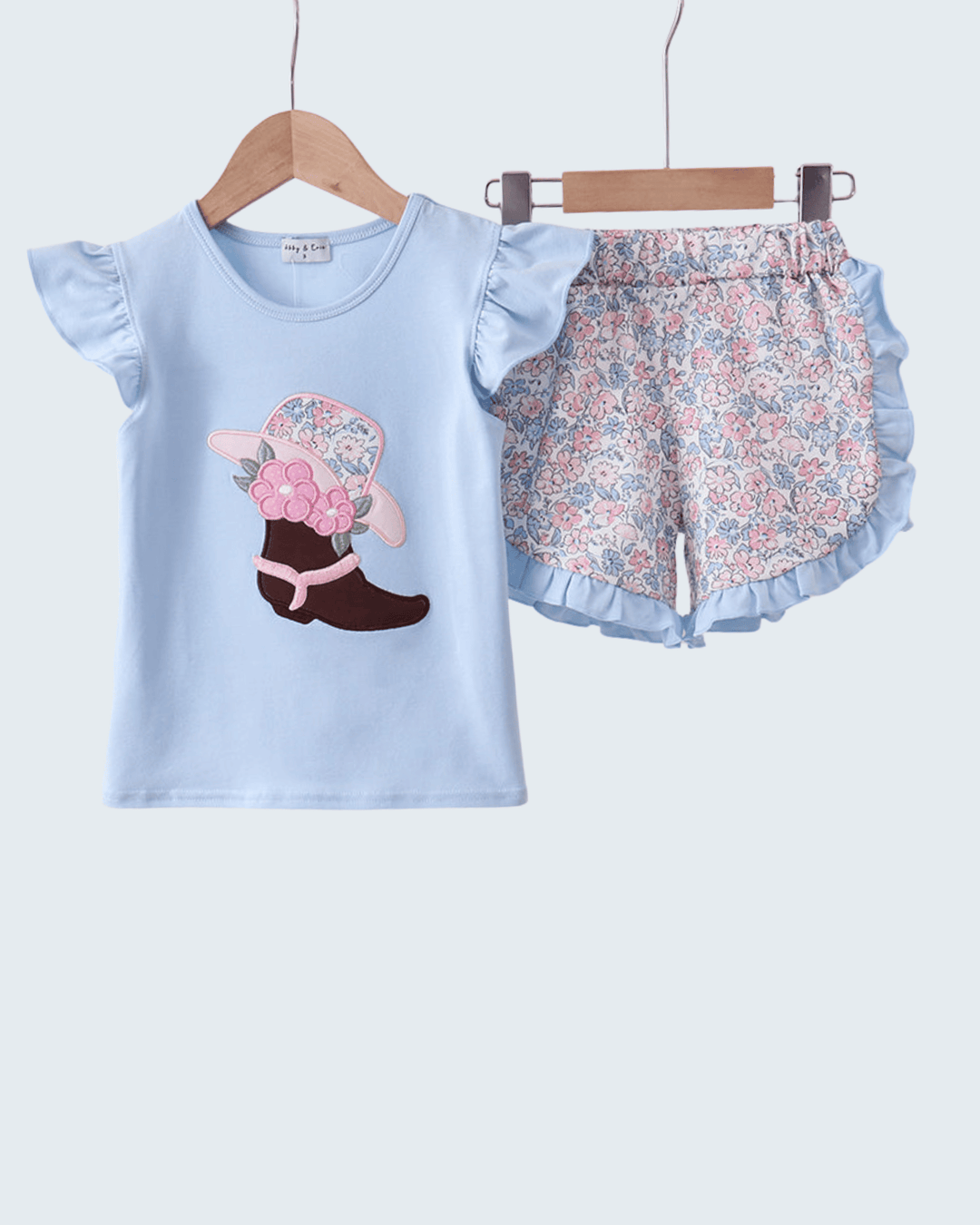 Children's outfit with blue top and floral shorts on hangers against a light gray background
