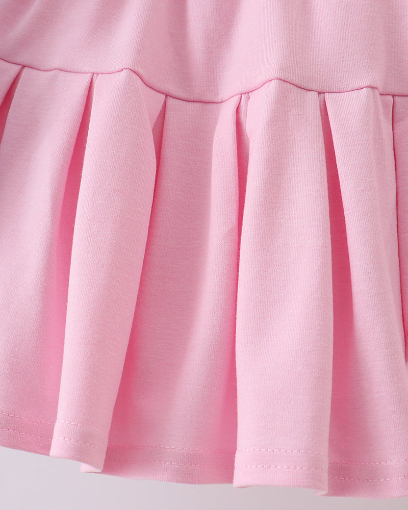 Close-up of a pink skirt with pleated details on a light gray background