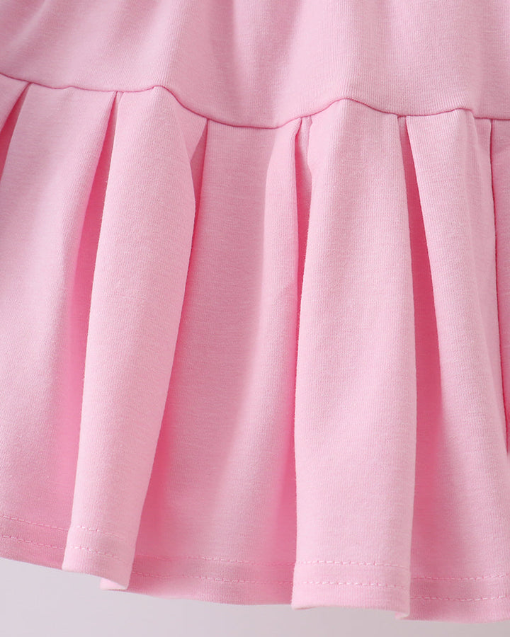 Close-up of a pink skirt with pleated details on a light gray background
