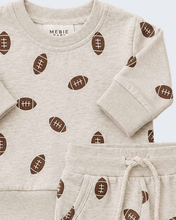 A baby long-sleeve sweatshirt and matching jogger pants set by Mebie Baby, featuring an all-over brown football print on a light heathered cream fabric.