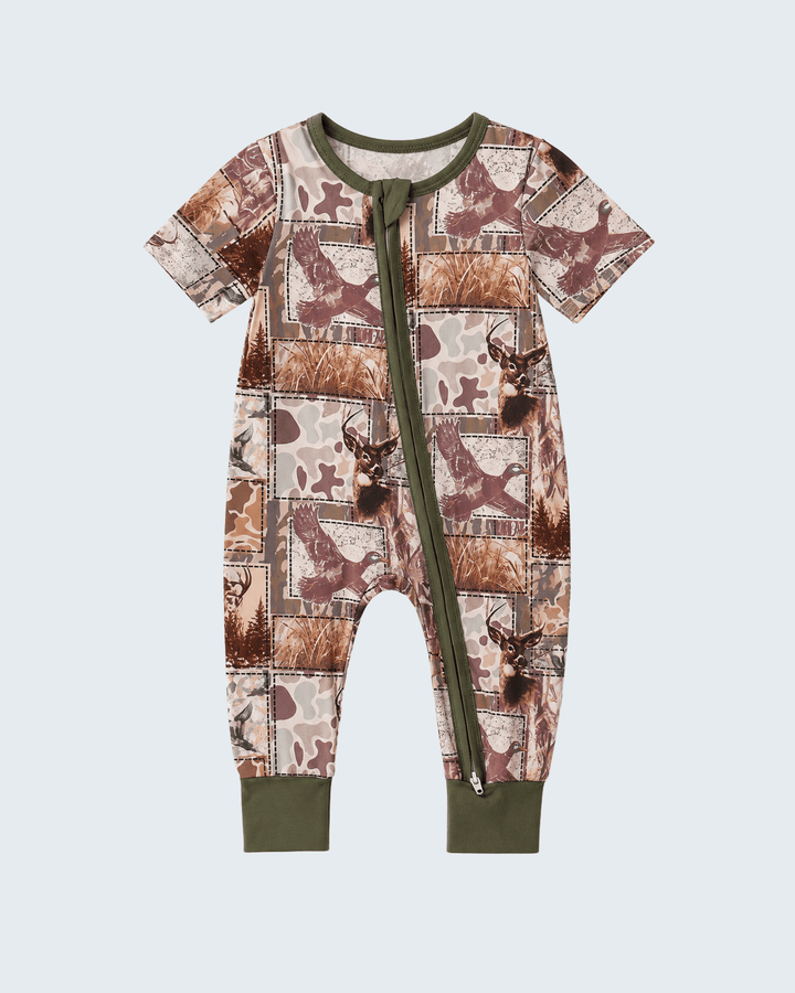 A baby short-sleeve footless one-piece romper with an allover patchwork print of brown deer and woodland camouflage motifs, featuring olive green trim, a front zipper, and ribbed cuffs.