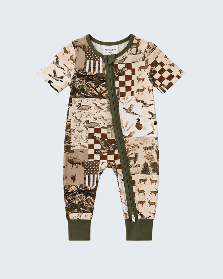 A baby short-sleeve footless one-piece jumpsuit with a green zipper, featuring a woodland-themed patchwork print in beige, brown, and green, shown on a light gray background.