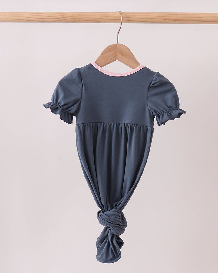 Dark blue smocked baby gown with puff sleeves, pink neckline trim, and knotted back
