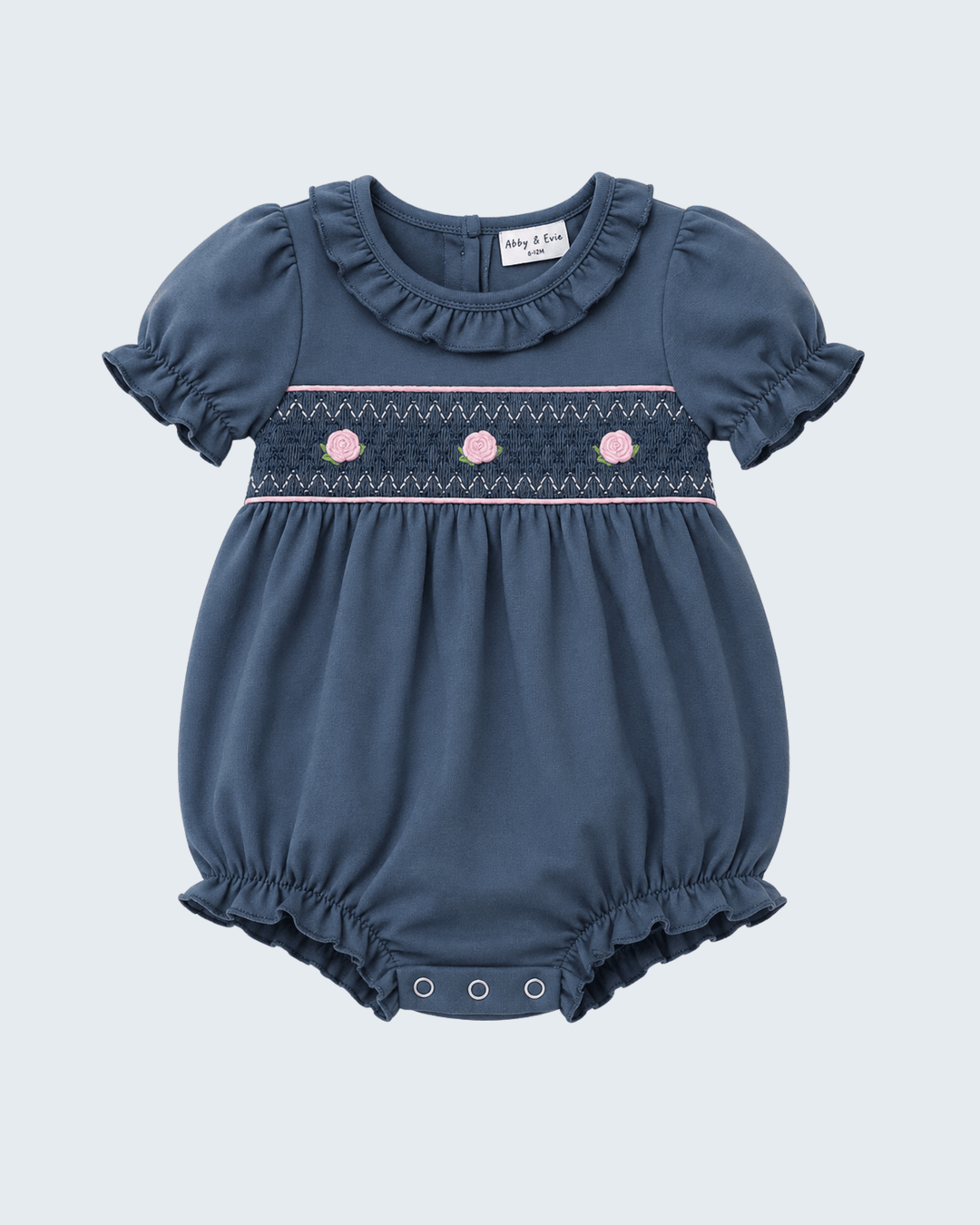 A baby girl's short-sleeve bubble romper in slate blue, featuring ruffled trim at the collar and leg hems, and a smocked chest band with pink floral details.