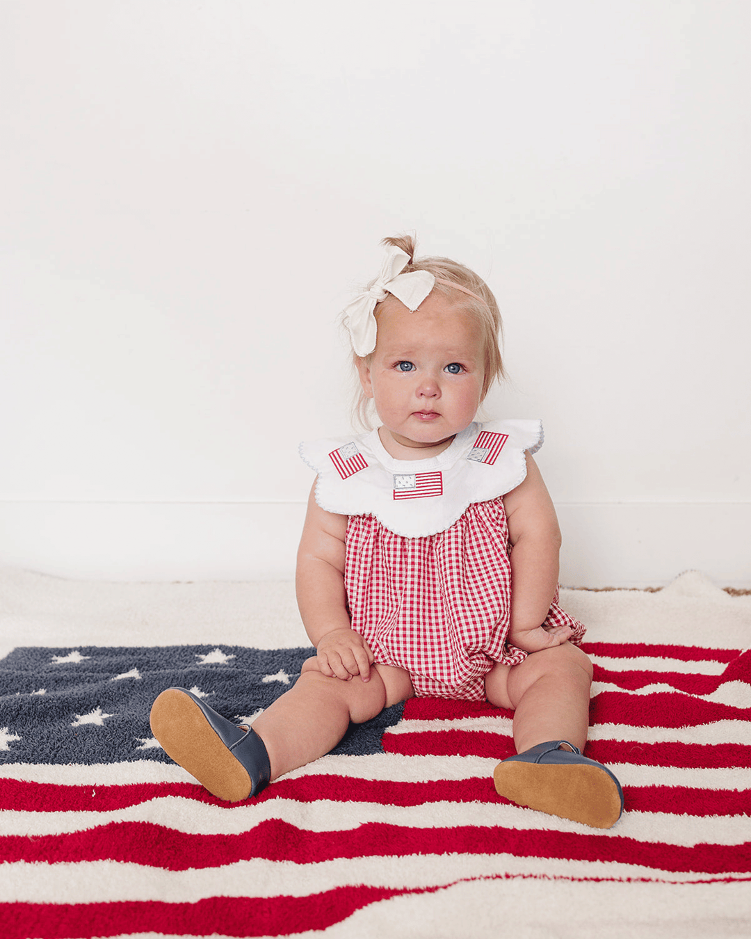 Baby sitting on an American flag with a white background