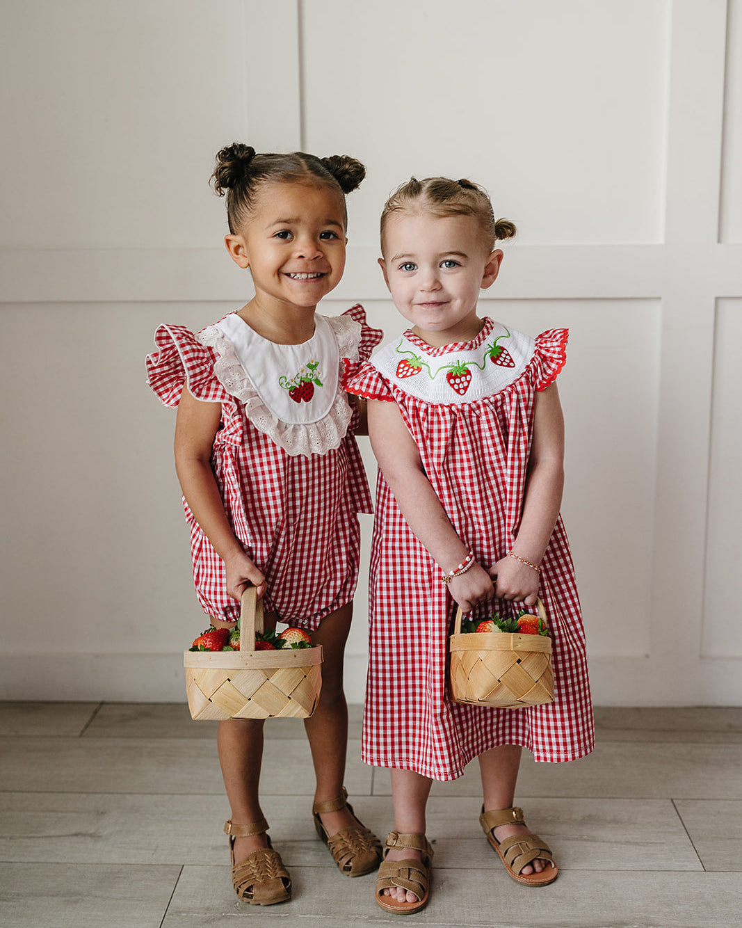 Two young girls in matching red and white checkered dresses holding small baskets.