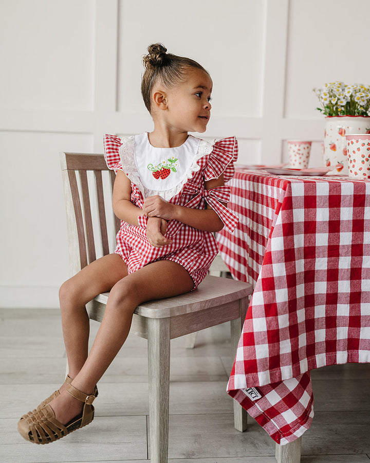 Child sitting at a table with a red and white checkered tablecloth, wearing a matching outfit.