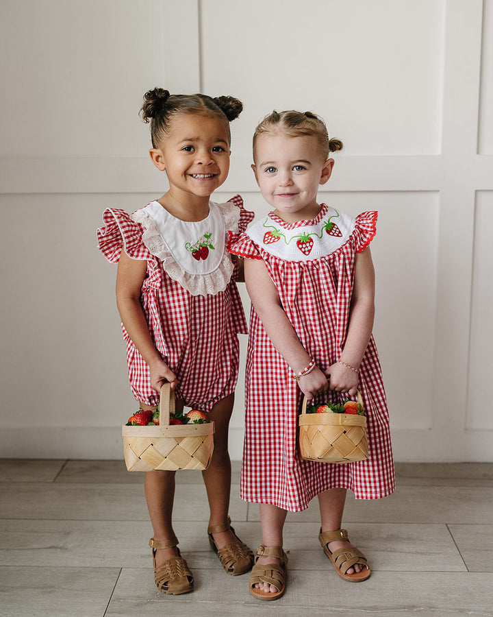 Two young girls in matching red and white checkered dresses holding small baskets.
