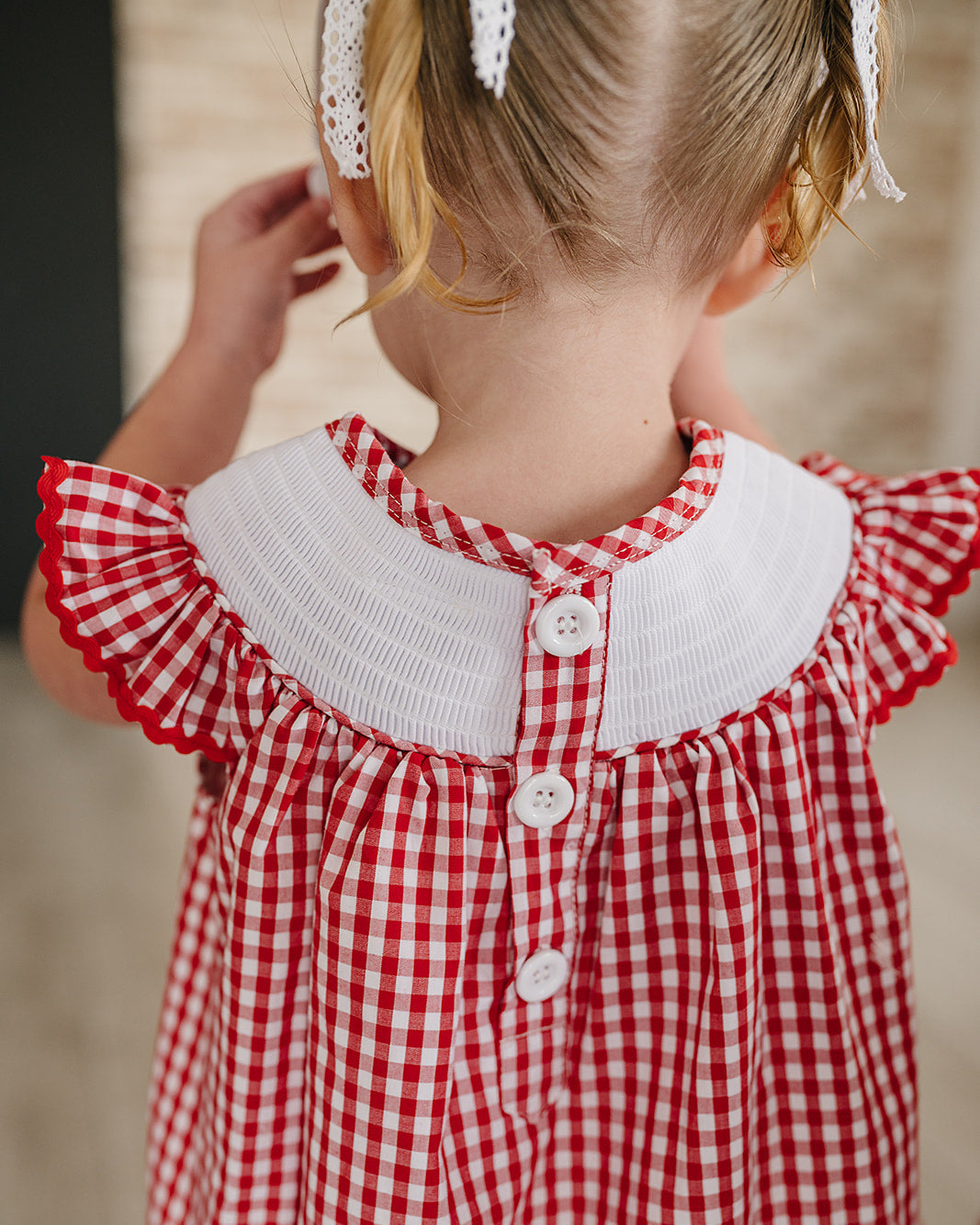 Child wearing a red and white checkered dress with a white collar.