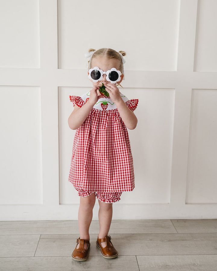 Child wearing a red checkered dress with a white wall background