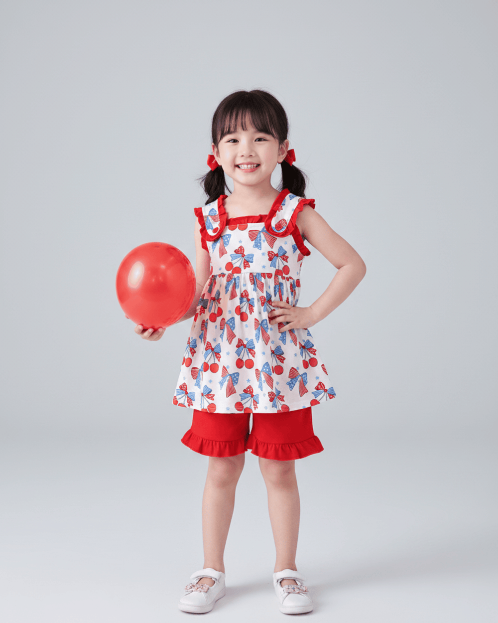 Young girl in a red and white dress holding a red balloon against a gray background