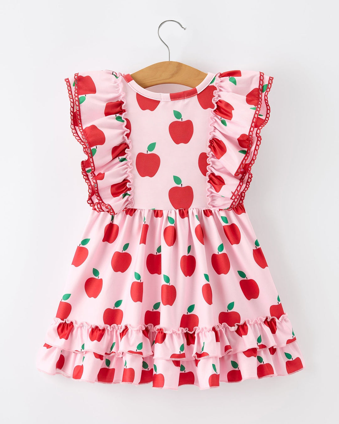 Pink dress with red apple pattern on a hanger against a white background