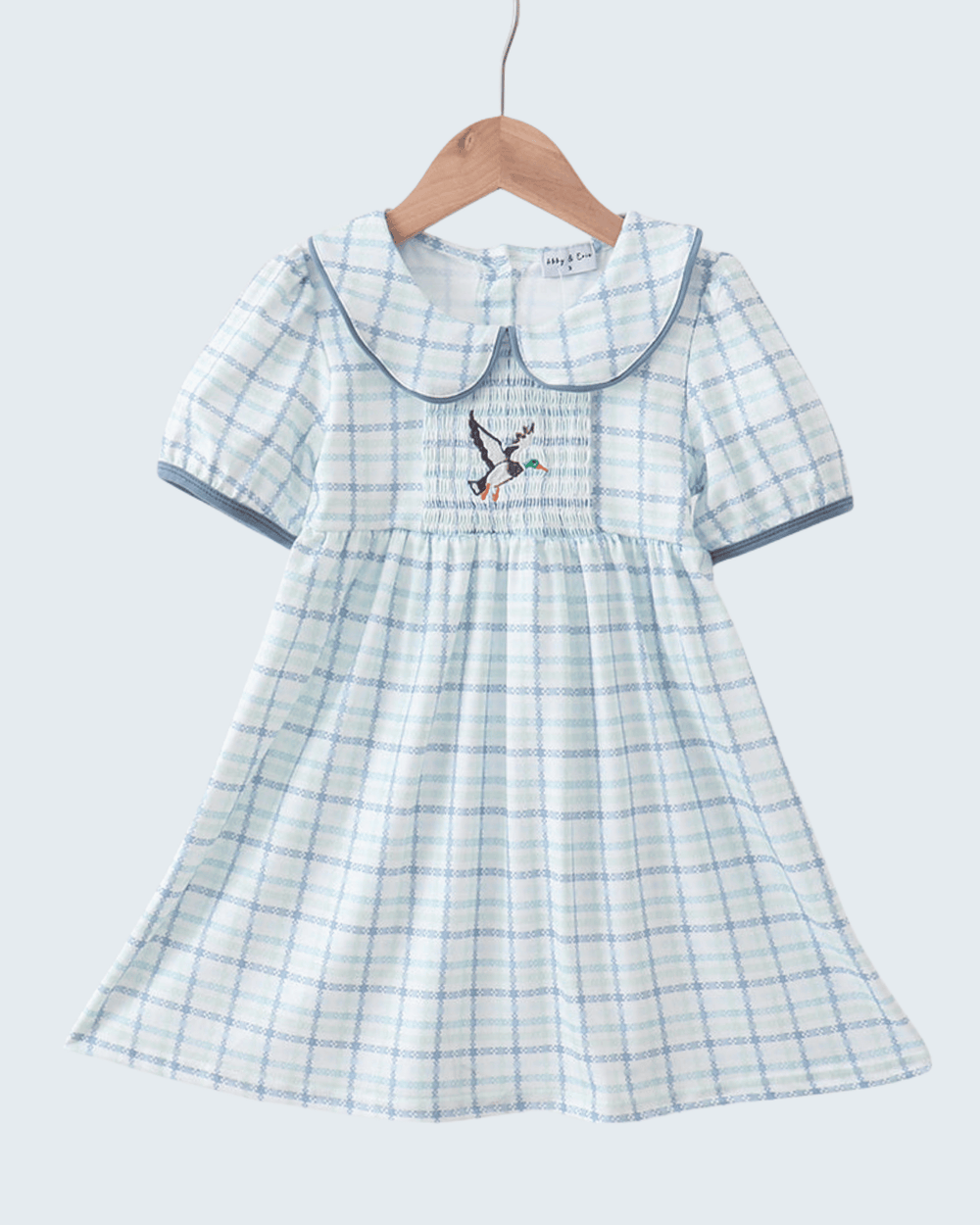 Plaid dress with a bird design on a hanger against a light gray background