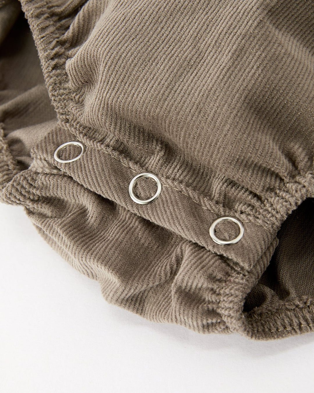 Close-up of a brown corduroy garment with three silver metal grommets on a white background.