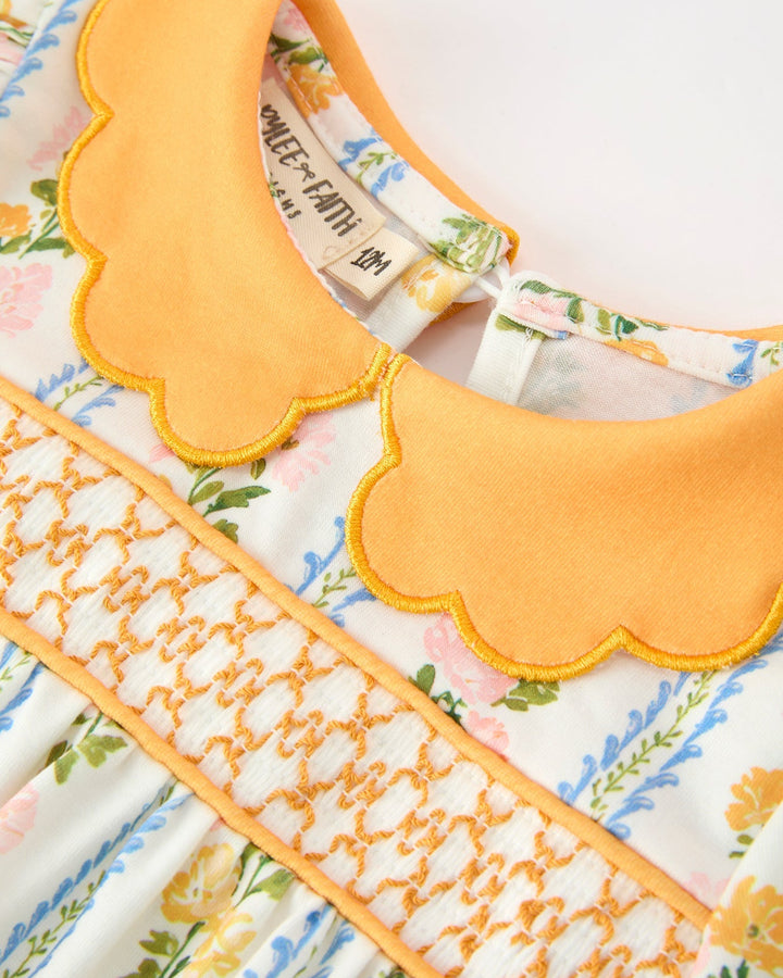 Close-up: orange scallop collar with layered ruffle trim on floral stripe baby romper.