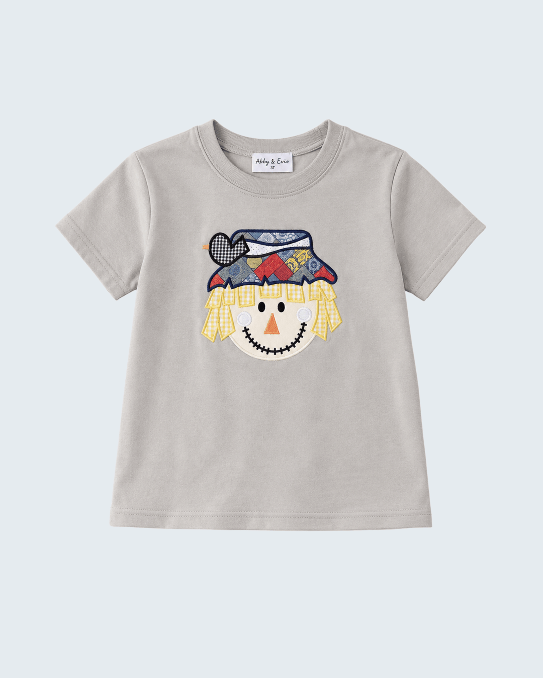 A light gray short-sleeve t-shirt for kids, featuring a colorful embroidered scarecrow face on the front. The shirt is displayed flat against a light gray background.
