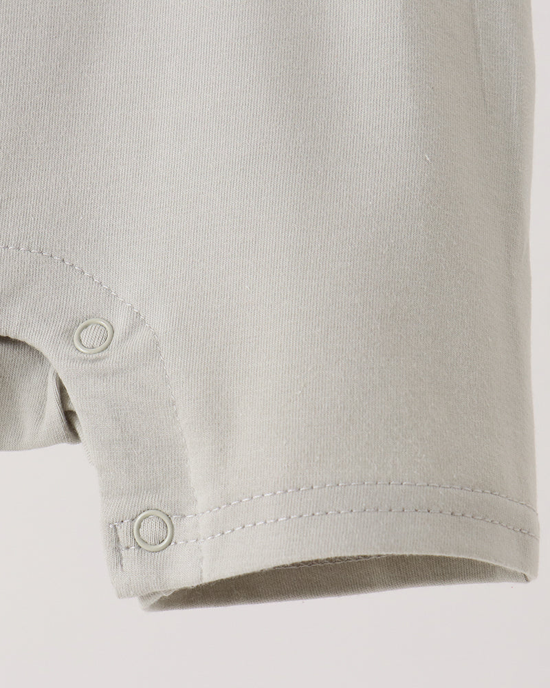 Close-up of a light gray or off-white baby garment sleeve with snap-button closure at the cuff, shown against a plain light background.