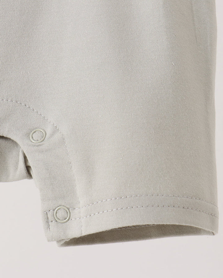 Close-up of a light gray or off-white baby garment sleeve with snap-button closure at the cuff, shown against a plain light background.