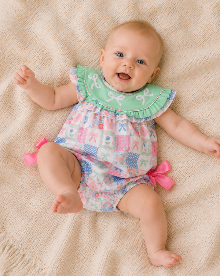 Baby wearing a colorful outfit with a green bib on a beige blanket