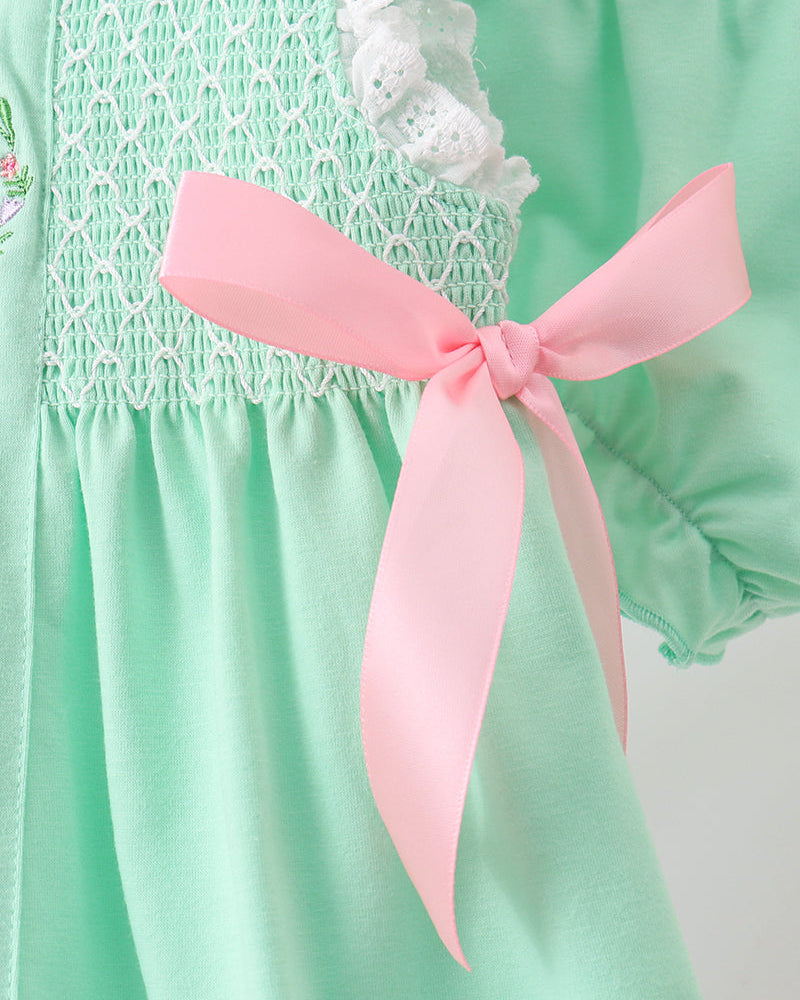 Green outfit with white lace and a pink ribbon on a plain background