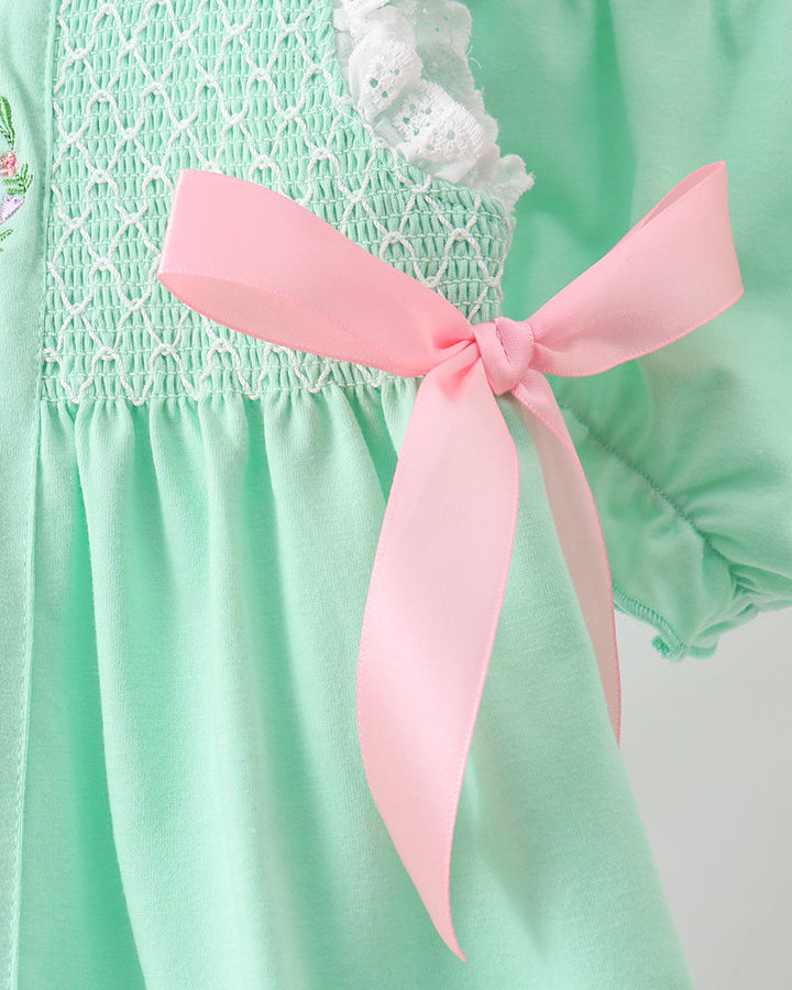 Green outfit with white lace and a pink ribbon on a plain background