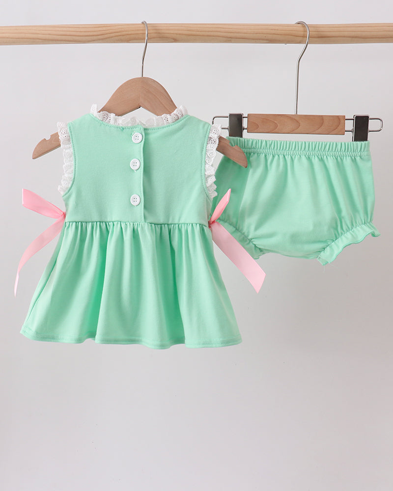Mint green baby dress with buttons and pink ribbons on a wooden hanger against a light gray background.