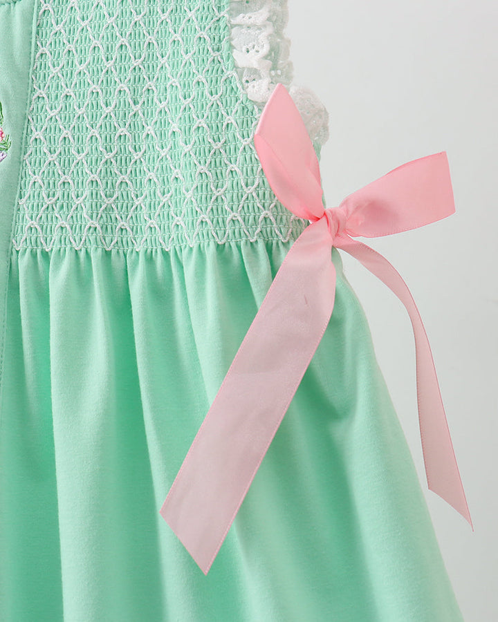 Green dress with white lace details and a pink ribbon on a plain background