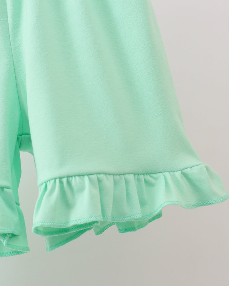 Close-up of a light green long-sleeve top with ruffled hem on a plain background